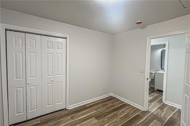 unfurnished bedroom with baseboards, dark wood-style flooring, and a closet