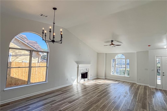 unfurnished living room with visible vents, dark wood-type flooring, ceiling fan with notable chandelier, a high end fireplace, and vaulted ceiling