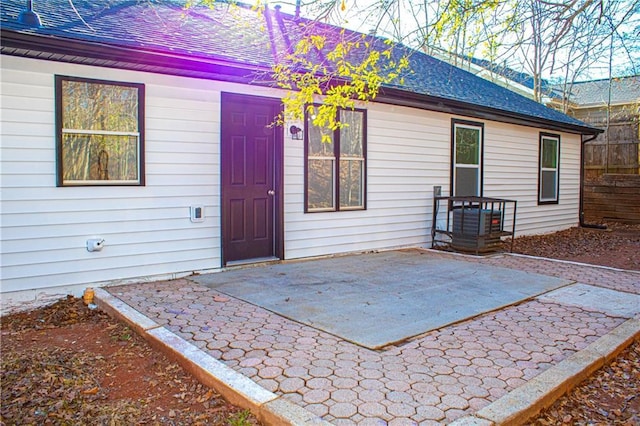 view of exterior entry with fence, a shingled roof, and a patio area