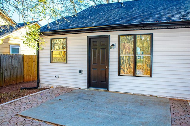 property entrance with a patio area, a shingled roof, and fence