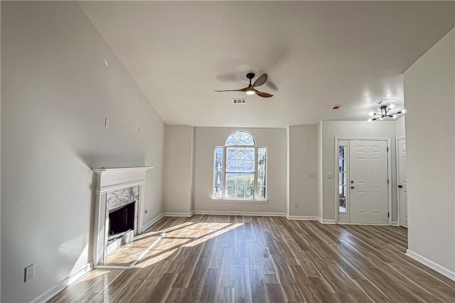 unfurnished living room featuring a high end fireplace, visible vents, baseboards, dark wood finished floors, and a ceiling fan