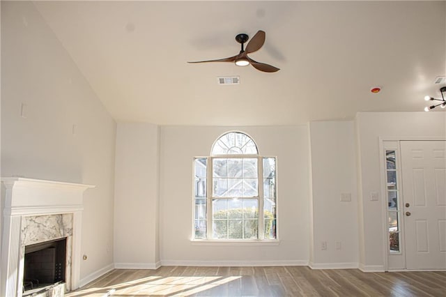 unfurnished living room with visible vents, wood finished floors, a premium fireplace, baseboards, and ceiling fan