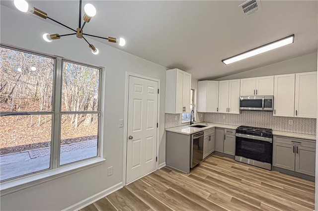 kitchen with lofted ceiling, gray cabinets, a sink, appliances with stainless steel finishes, and a chandelier