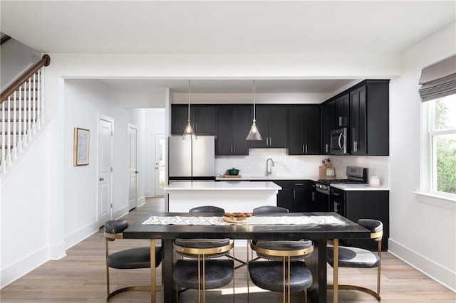 kitchen featuring sink, light hardwood / wood-style flooring, appliances with stainless steel finishes, tasteful backsplash, and decorative light fixtures