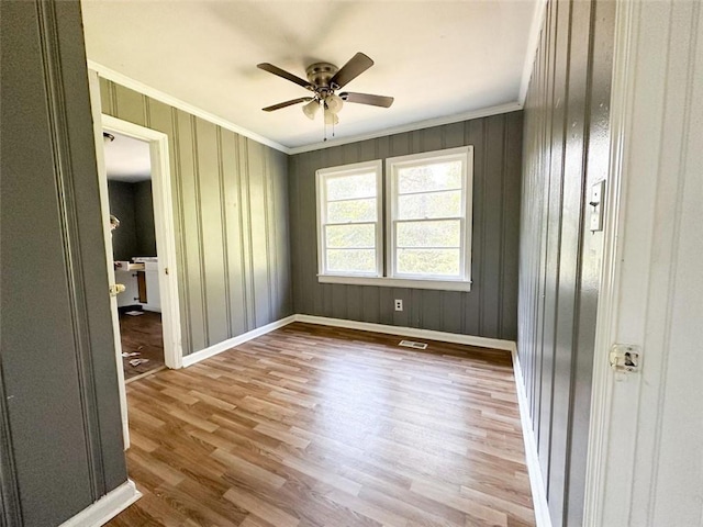 spare room with visible vents, ornamental molding, a ceiling fan, wood finished floors, and baseboards