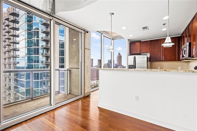 kitchen with appliances with stainless steel finishes, light wood-style floors, expansive windows, light stone countertops, and pendant lighting