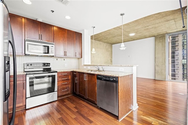 kitchen featuring appliances with stainless steel finishes, dark wood finished floors, a sink, a peninsula, and light stone counters