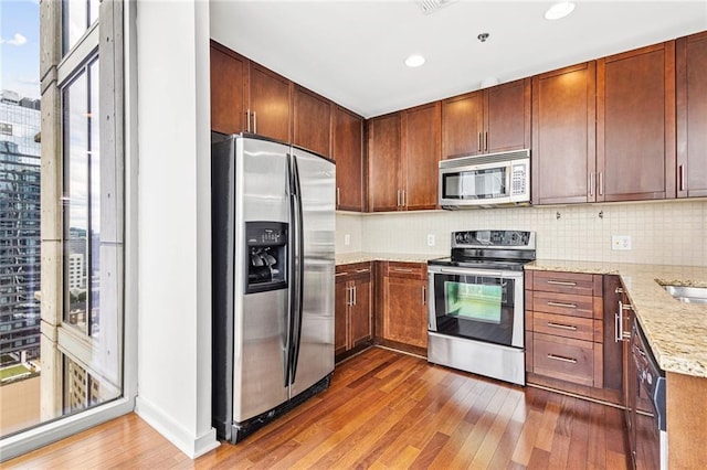 kitchen with appliances with stainless steel finishes, hardwood / wood-style flooring, plenty of natural light, backsplash, and recessed lighting