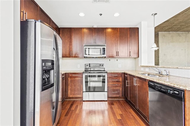 kitchen with appliances with stainless steel finishes, a sink, dark wood finished floors, light stone counters, and backsplash