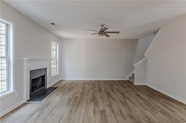 unfurnished living room featuring wood finished floors, a fireplace with raised hearth, plenty of natural light, and stairs