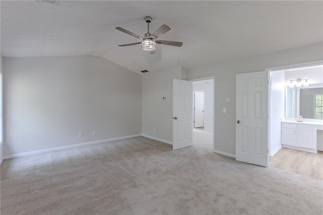 unfurnished bedroom with lofted ceiling, light carpet, connected bathroom, ceiling fan, and baseboards