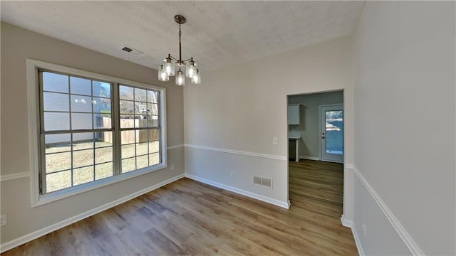 unfurnished dining area with an inviting chandelier, wood-type flooring, and a textured ceiling