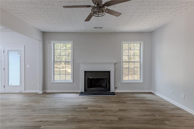 unfurnished living room with a textured ceiling, a fireplace, wood finished floors, and visible vents