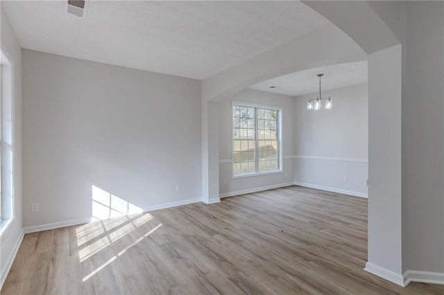 spare room featuring baseboards, visible vents, arched walkways, and wood finished floors