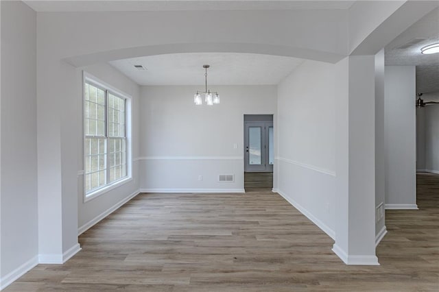 unfurnished dining area with arched walkways, baseboards, wood finished floors, and a notable chandelier