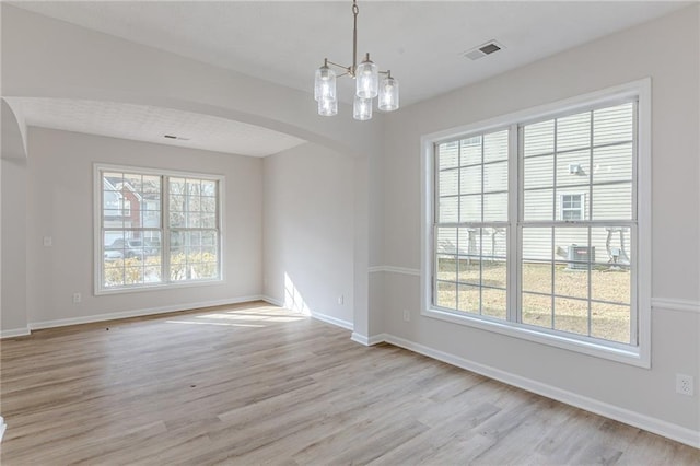 spare room featuring arched walkways, light wood-style flooring, plenty of natural light, and visible vents