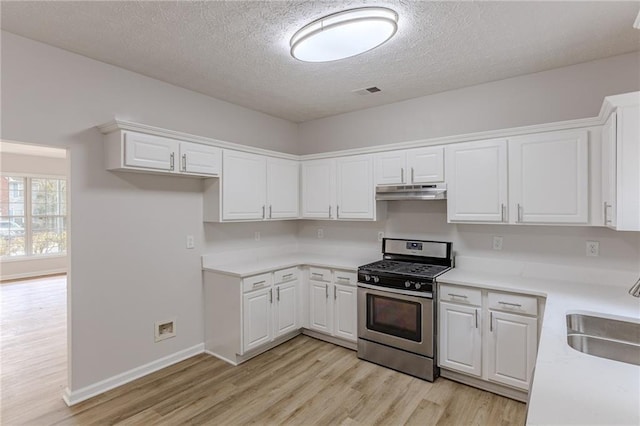 kitchen with under cabinet range hood, a sink, white cabinets, light wood finished floors, and gas stove