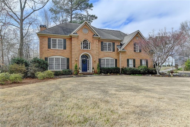 georgian-style home featuring brick siding, a chimney, and a front yard