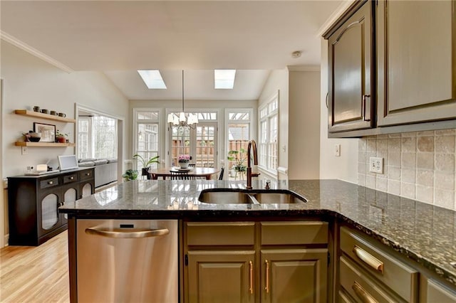 kitchen with a peninsula, a sink, stainless steel dishwasher, dark stone counters, and tasteful backsplash