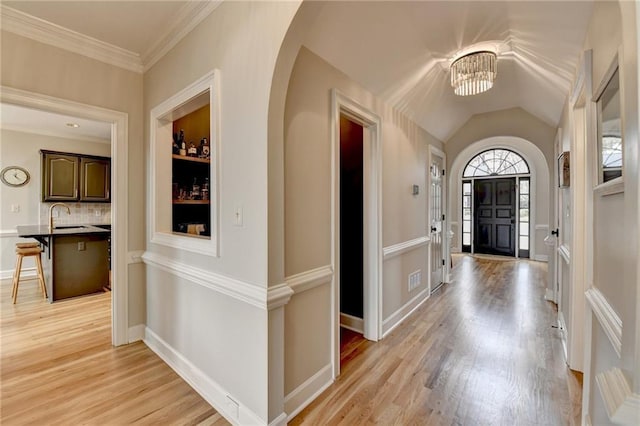 foyer entrance with arched walkways, vaulted ceiling, light wood-type flooring, and a chandelier