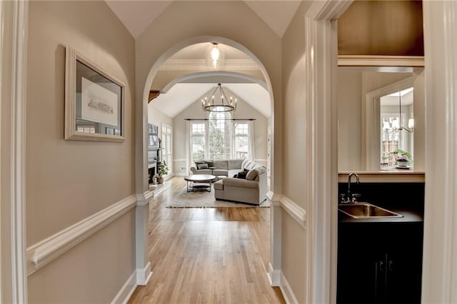 hallway featuring light wood finished floors, baseboards, lofted ceiling, an inviting chandelier, and a sink