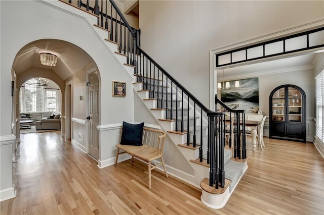 staircase featuring baseboards, arched walkways, ornamental molding, wood finished floors, and a notable chandelier