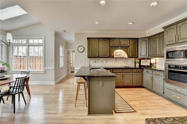 kitchen featuring stainless steel appliances, a sink, light wood-style floors, backsplash, and dark stone countertops