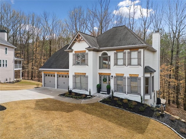 view of front facade with a front lawn, roof with shingles, a chimney, a garage, and driveway