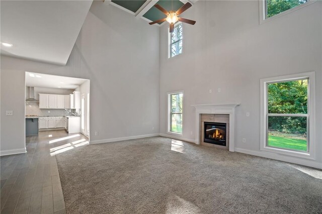 unfurnished living room with ceiling fan, baseboards, a high ceiling, and a glass covered fireplace