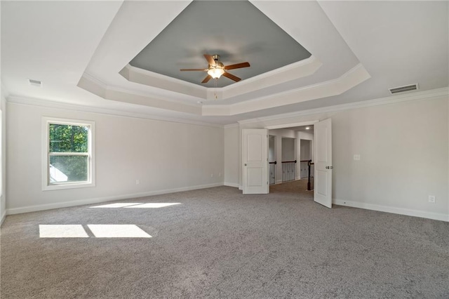 unfurnished bedroom with a tray ceiling, carpet, visible vents, and ornamental molding
