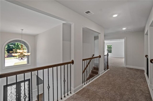 corridor with visible vents, an upstairs landing, carpet floors, and a notable chandelier