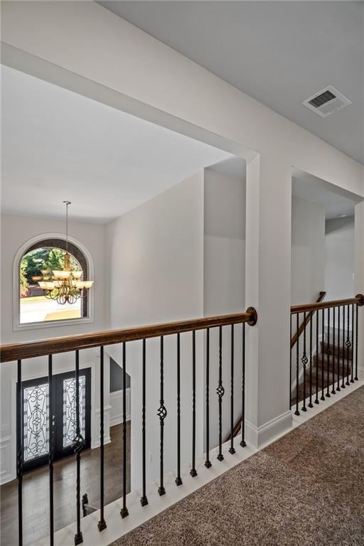 corridor with carpet flooring, a notable chandelier, an upstairs landing, and visible vents