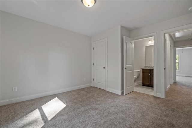 unfurnished bedroom featuring baseboards, ensuite bath, attic access, and light colored carpet