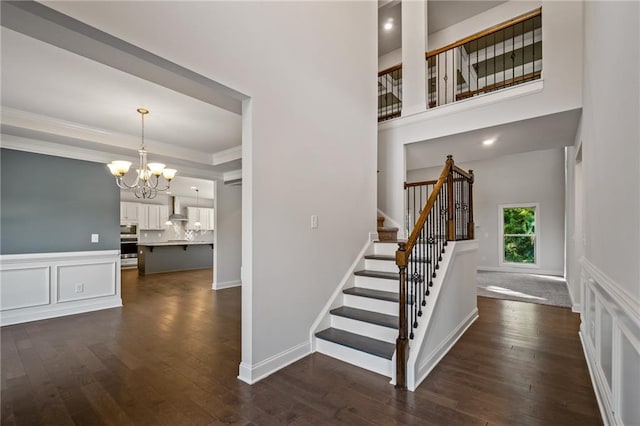 staircase featuring a decorative wall, wood finished floors, ornamental molding, wainscoting, and a notable chandelier