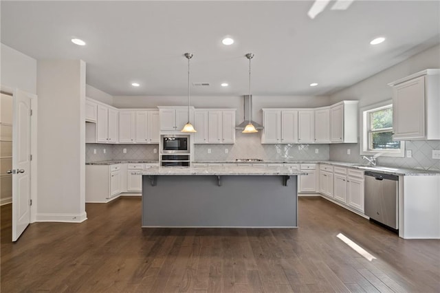 kitchen with wall chimney range hood, stainless steel appliances, white cabinets, and a kitchen island