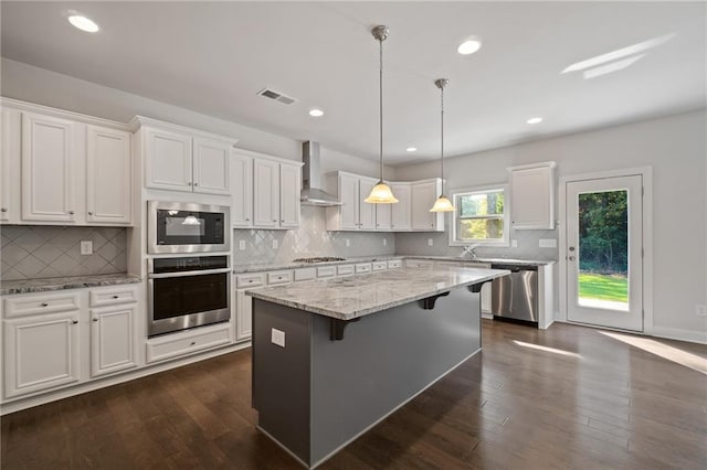 kitchen featuring a center island, visible vents, wall chimney exhaust hood, white cabinets, and appliances with stainless steel finishes