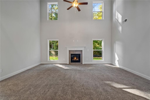 unfurnished living room featuring carpet flooring, a wealth of natural light, visible vents, and a high ceiling