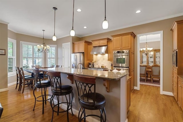 kitchen featuring under cabinet range hood, stainless steel appliances, a chandelier, and light wood-style flooring