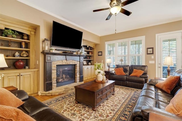 living room featuring ceiling fan, a stone fireplace, wood finished floors, and ornamental molding