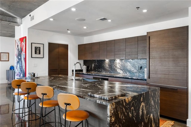 kitchen featuring a breakfast bar, a sink, visible vents, and tasteful backsplash