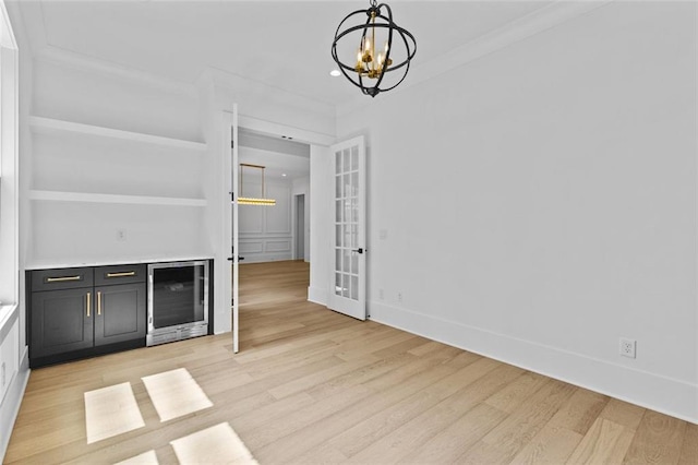 interior space featuring light wood finished floors, a chandelier, baseboards, wine cooler, and ornamental molding