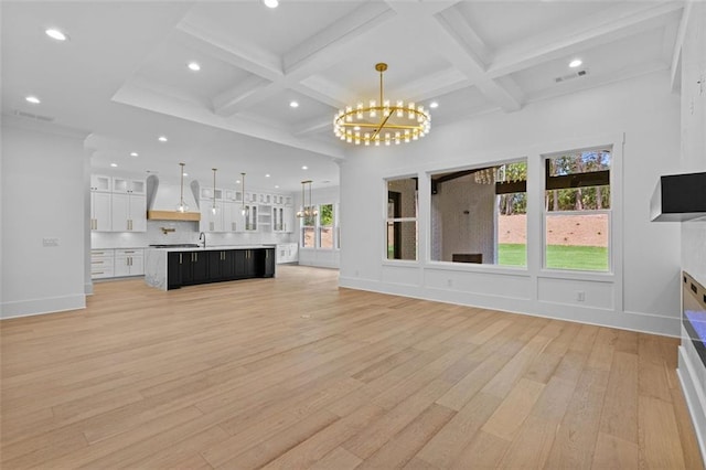 unfurnished living room with an inviting chandelier, light wood-style flooring, visible vents, and beamed ceiling