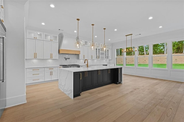 kitchen with light wood-style floors, white cabinetry, a kitchen island with sink, and premium range hood