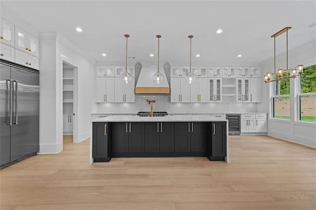 kitchen with light countertops, built in refrigerator, white cabinets, wine cooler, and custom range hood