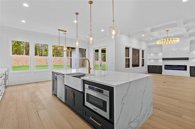kitchen with stainless steel dishwasher, a kitchen island with sink, recessed lighting, a sink, and light wood finished floors