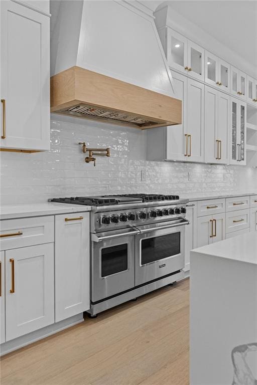 kitchen with light countertops, range with two ovens, white cabinetry, backsplash, and custom exhaust hood