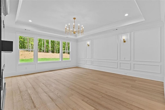 interior space with a tray ceiling, light wood finished floors, an inviting chandelier, a decorative wall, and a wealth of natural light