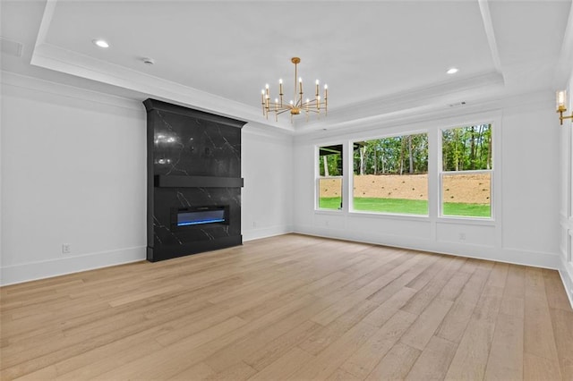 unfurnished living room featuring crown molding, an inviting chandelier, light wood-style flooring, and a raised ceiling