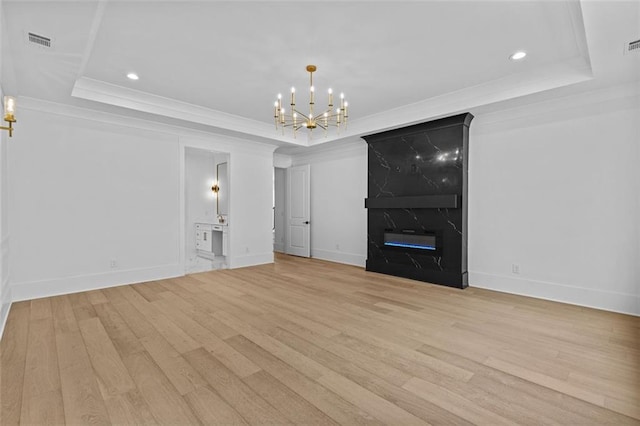 unfurnished living room featuring a chandelier, visible vents, light wood finished floors, and a raised ceiling