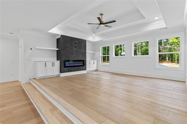 unfurnished living room featuring crown molding, a high end fireplace, a raised ceiling, a ceiling fan, and light wood-style flooring